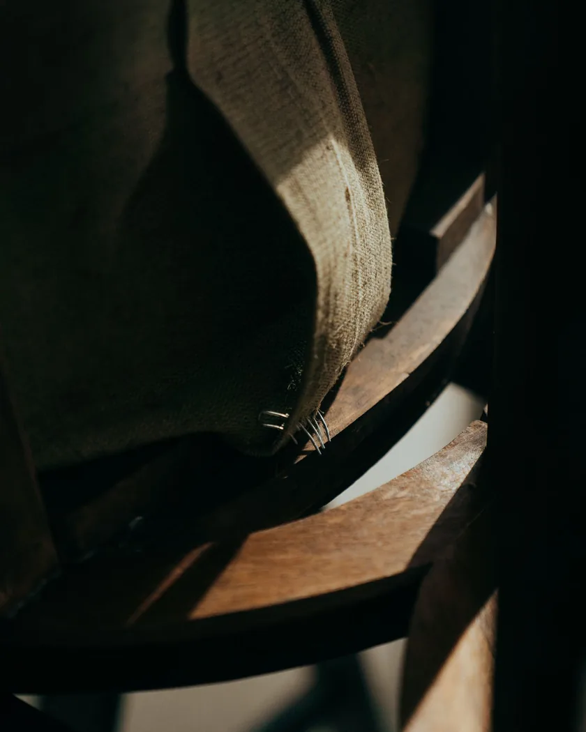 Detalle de la tela de refuerzo grapada al travesaño de madera de una silla, con las grapas a la vista
