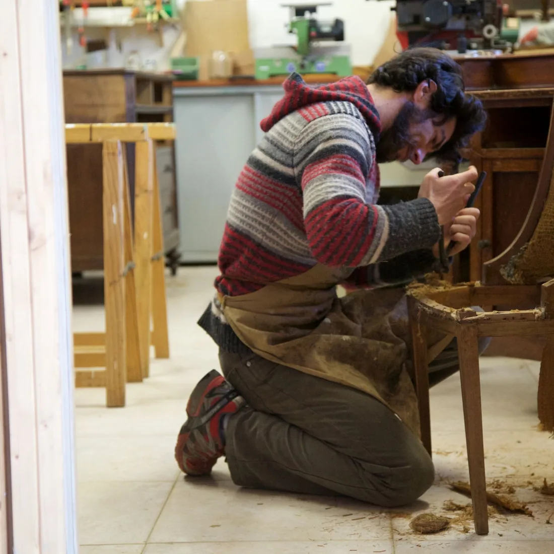 Una persona arrodillada retira el relleno de crin del asiento de una silla desmontada en un taller de tapicería